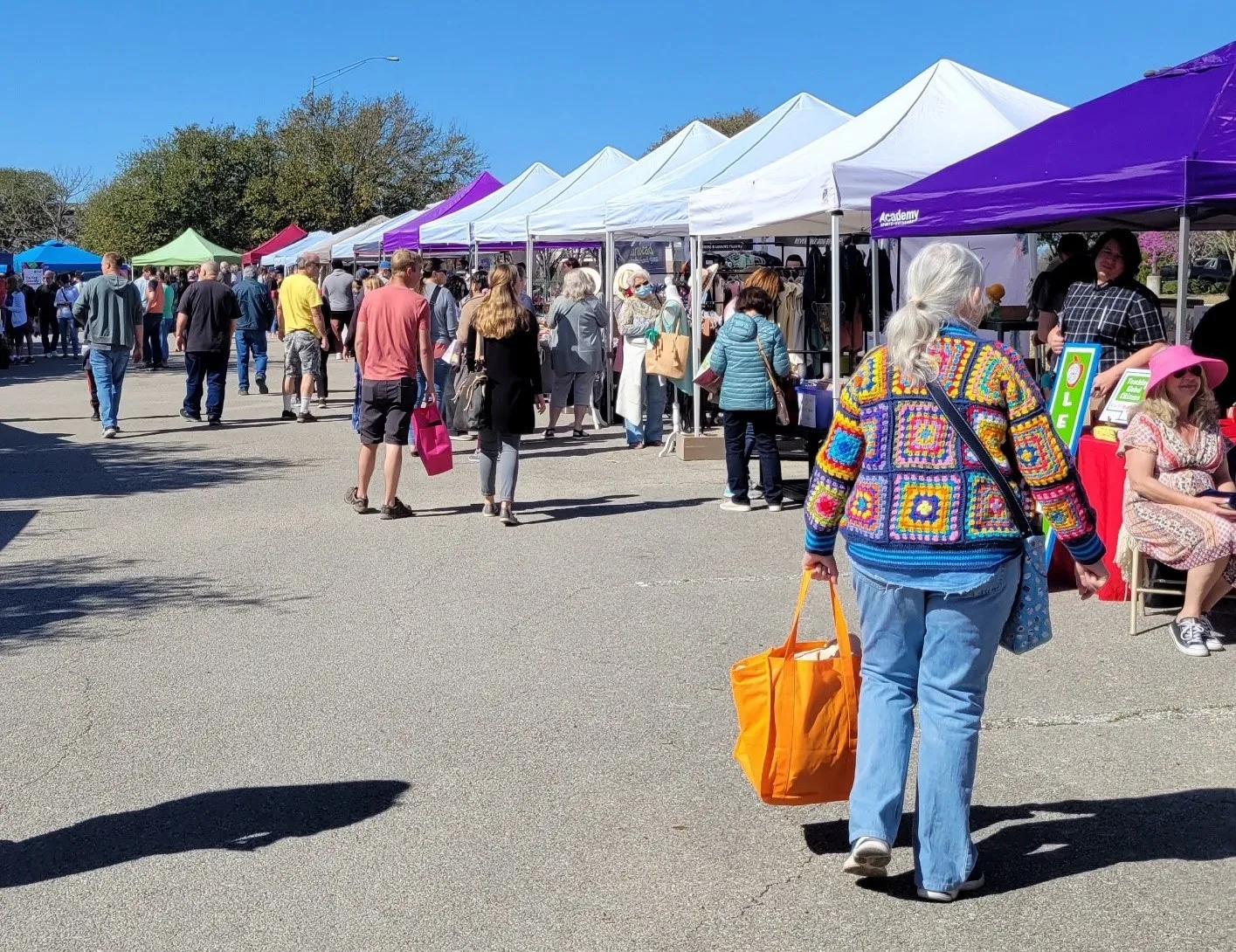 shoppers at farmers market with purple and white tents