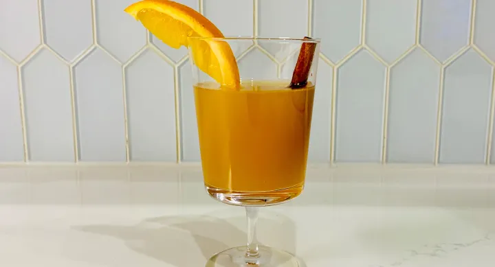 glass with cider garnished with orange slice and cinnamon stick